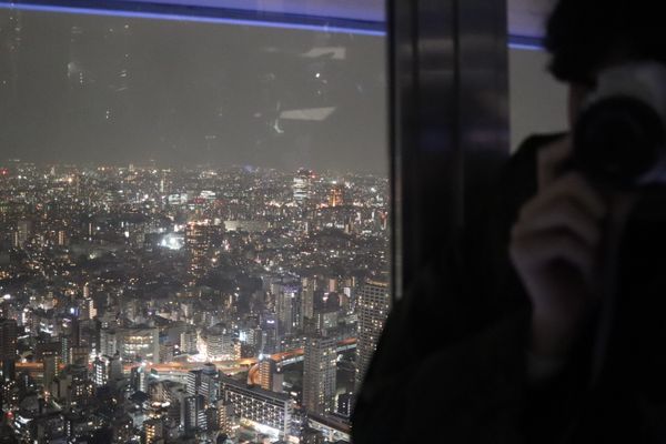 in the foreground person with a camera pointed at the lens, The background is the Tokyo Skyline, thumbnail