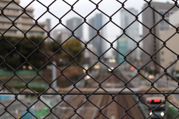 View of train tracks, through chain-link fence, out of focus train coming down the tracks., thumbnail